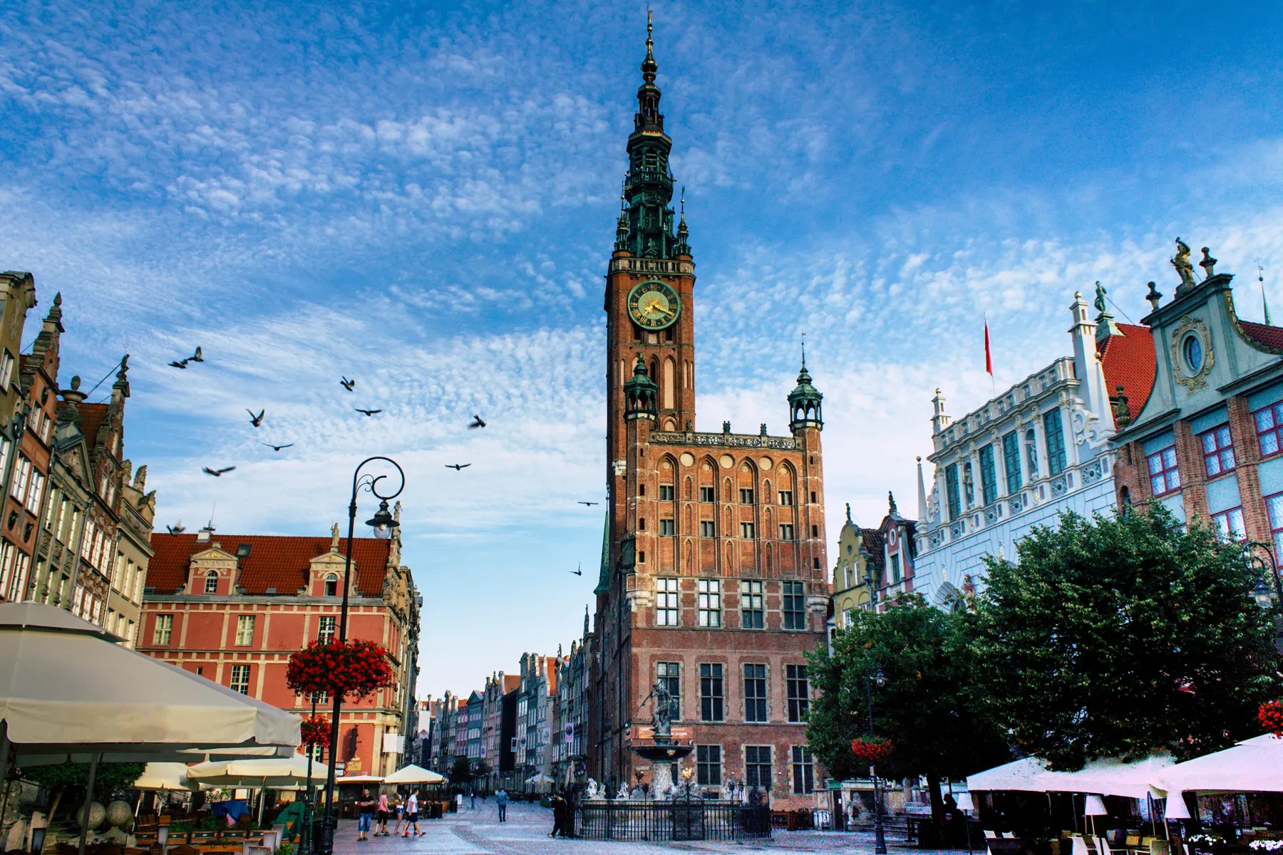 Ayuntamiento Principal de Gdansk, edificio de ladrillo rojo con torre de reloj alta, en una plaza animada con gente y fuente.