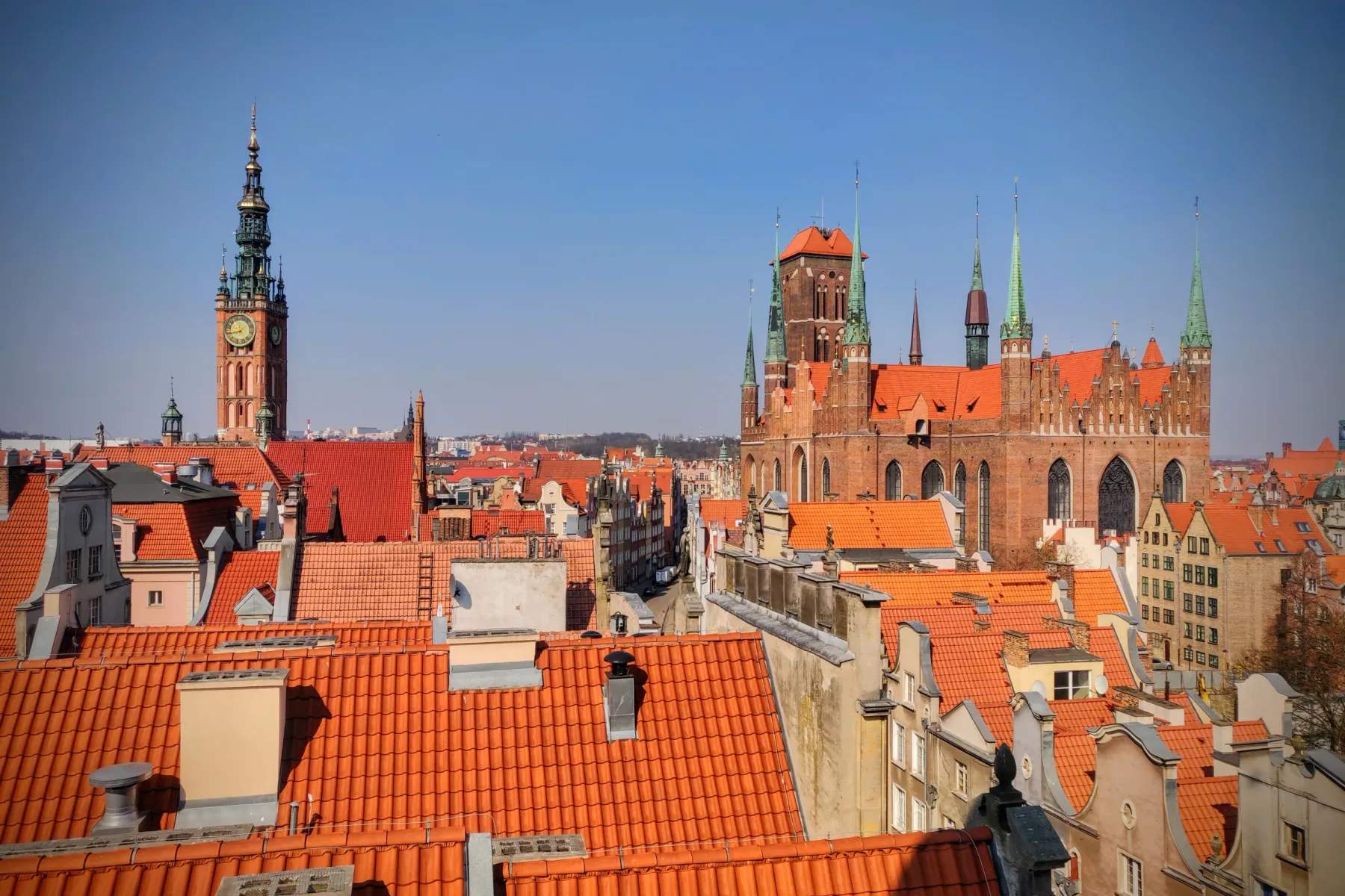 Erhöhter Blick auf Danzig mit dem Uhrenturm des Rechtstädtischen Rathauses und der Marienkirche, umgeben von roten Dächern.