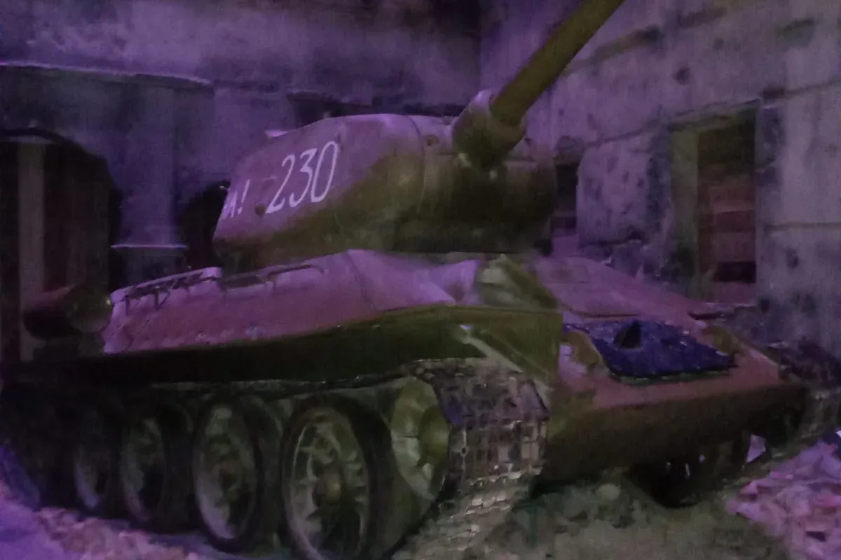 Ein T-34 Panzer mit der Nummer '230' auf dem Turm, umgeben von Schutt in einer dunklen, zerstörten Gebäudeausstellung.