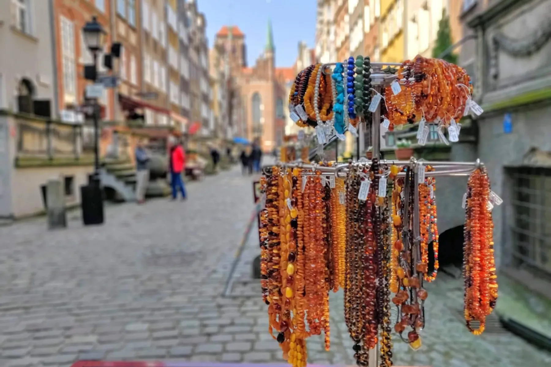 Ein Straßenstand mit zahlreichen Bernstein-Halsketten und Armbändern in verschiedenen Farbtönen, dahinter eine unscharfe A...