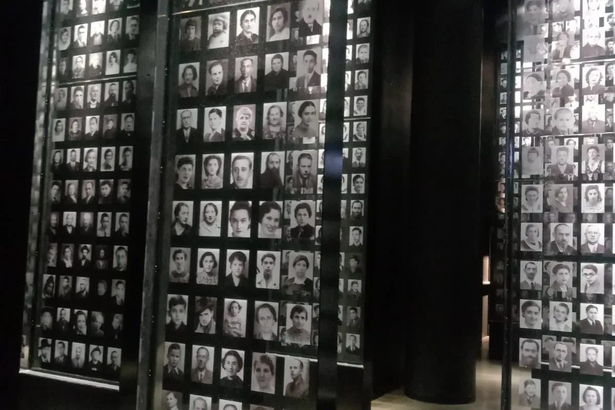 Dunkler Museumsraum mit hohen, beleuchteten Vitrinen, gefüllt mit kleinen Schwarz-Weiß-Porträts von Personen.