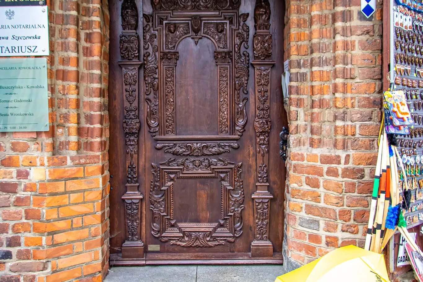 Reich geschnitzte dunkle Holztür in einem Backsteingebäude, mit gelbem Walkative-Regenschirm auf Kopfsteinpflaster in Toruń.