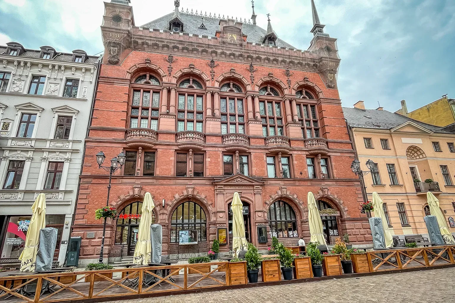 Prächtiges rotes Backsteingebäude mit Türmchen und Bogenfenstern in der Altstadt von Toruń, mit Außengastronomie und Sonne...