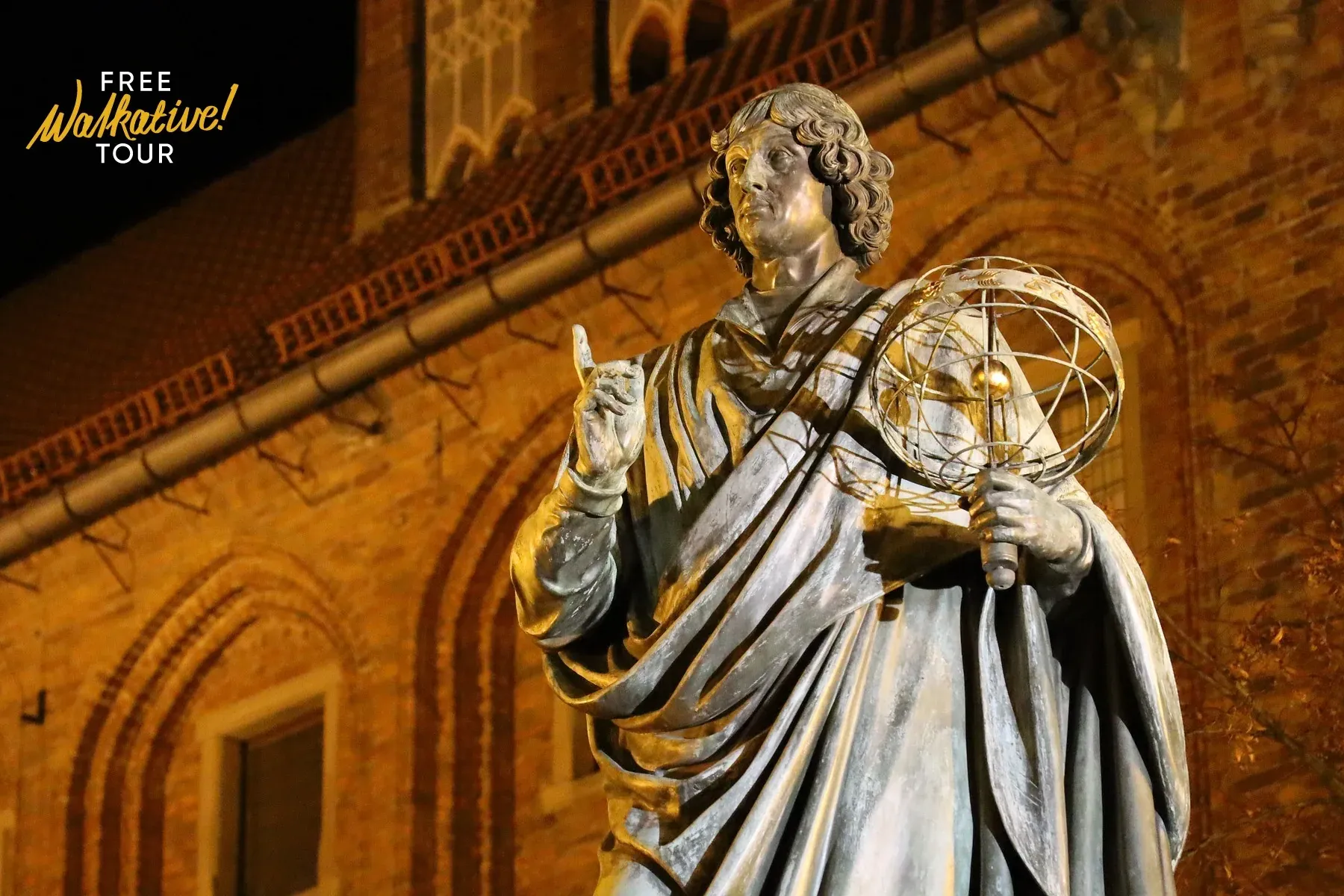 Bronzestatue von Nikolaus Kopernikus mit Armillarsphäre, nachts vor einem Backsteingebäude beleuchtet.