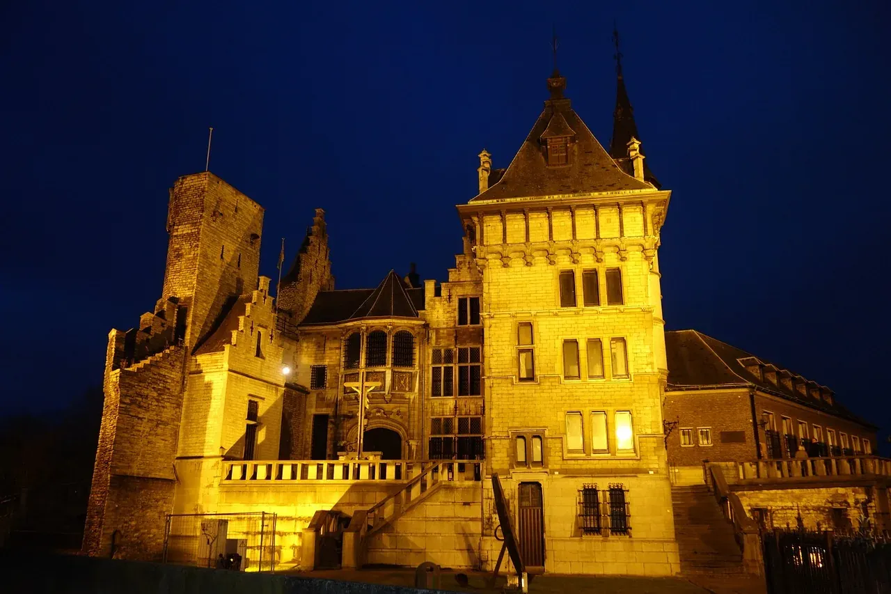 Gravensteen Schloss in Gent bei Nacht, warm beleuchtet, mit Steinmauern, einem quadratischen Turm und Giebeldächern unter ...