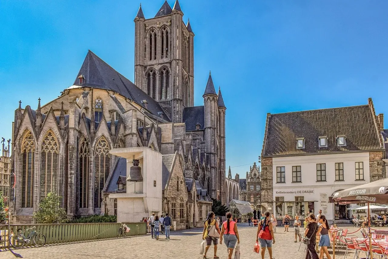 Histórica Iglesia de San Nicolás con su alto campanario, un edificio tradicional y gente caminando en una soleada plaza ad...