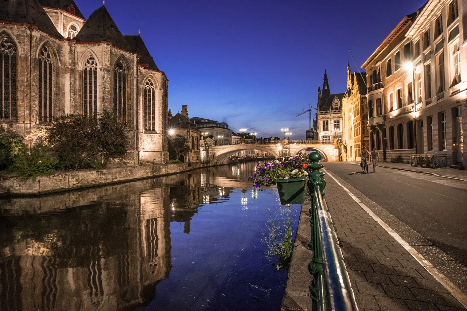 View of St. Michael's Bridge and Leie River in Ghent at dusk, with St. Michael's Church on the left, illuminated buildings...