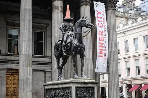 Reiterstatue des Herzogs von Wellington in Glasgow mit einem orangefarbenen Verkehrskegel auf dem Kopf, vor einem klassisc...