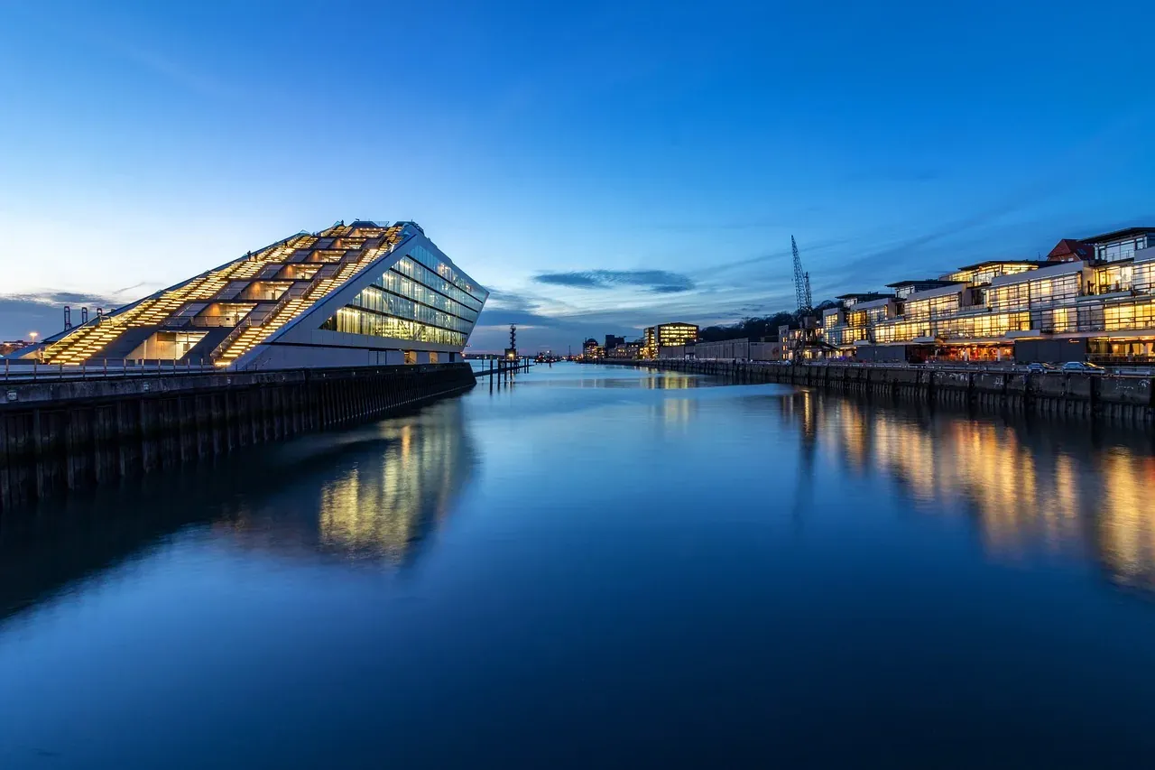 El moderno auditorio Elbphilharmonie y edificios ribereños iluminados al anochecer, reflejados en las tranquilas aguas del...