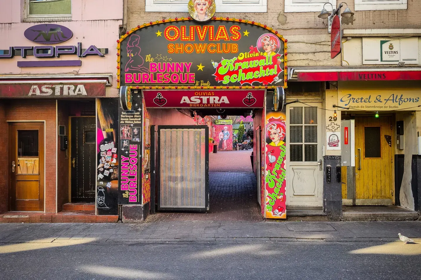 Entrada a Olivia's Showclub en Hamburgo, con un letrero de neón brillante y caricaturas, flanqueada por Utopia y Gretel & ...