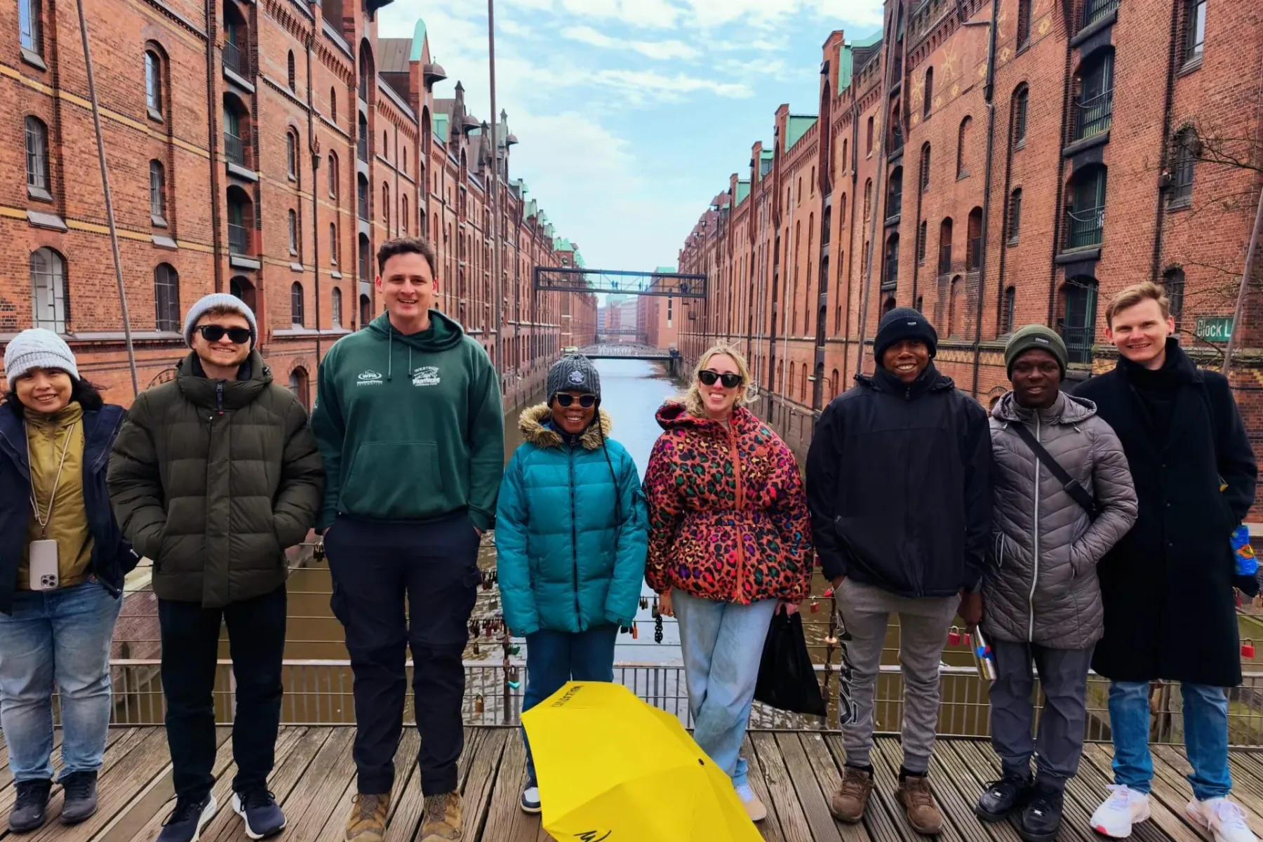 Grupo de turistas y guía en puente de madera en Speicherstadt, Hamburgo, con almacenes de ladrillo rojo y un canal.