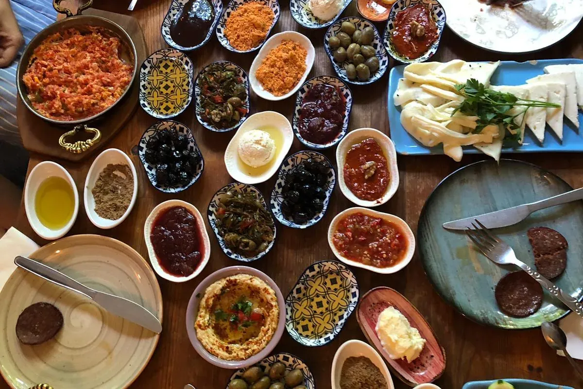 Vista superior de una gran mesa de madera con un desayuno turco tradicional: varios platos pequeños de salsas, aceitunas, ...