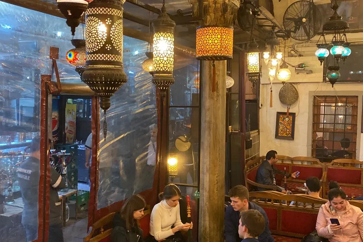 Personas relajándose en una casa de té tradicional de Estambul con lámparas colgantes de mosaico y filigrana.