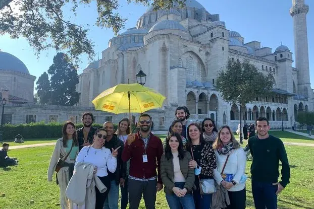 Un grupo de personas de pie en un césped frente a la gran Mezquita Süleymaniye con cúpula y su minarete en Estambul.