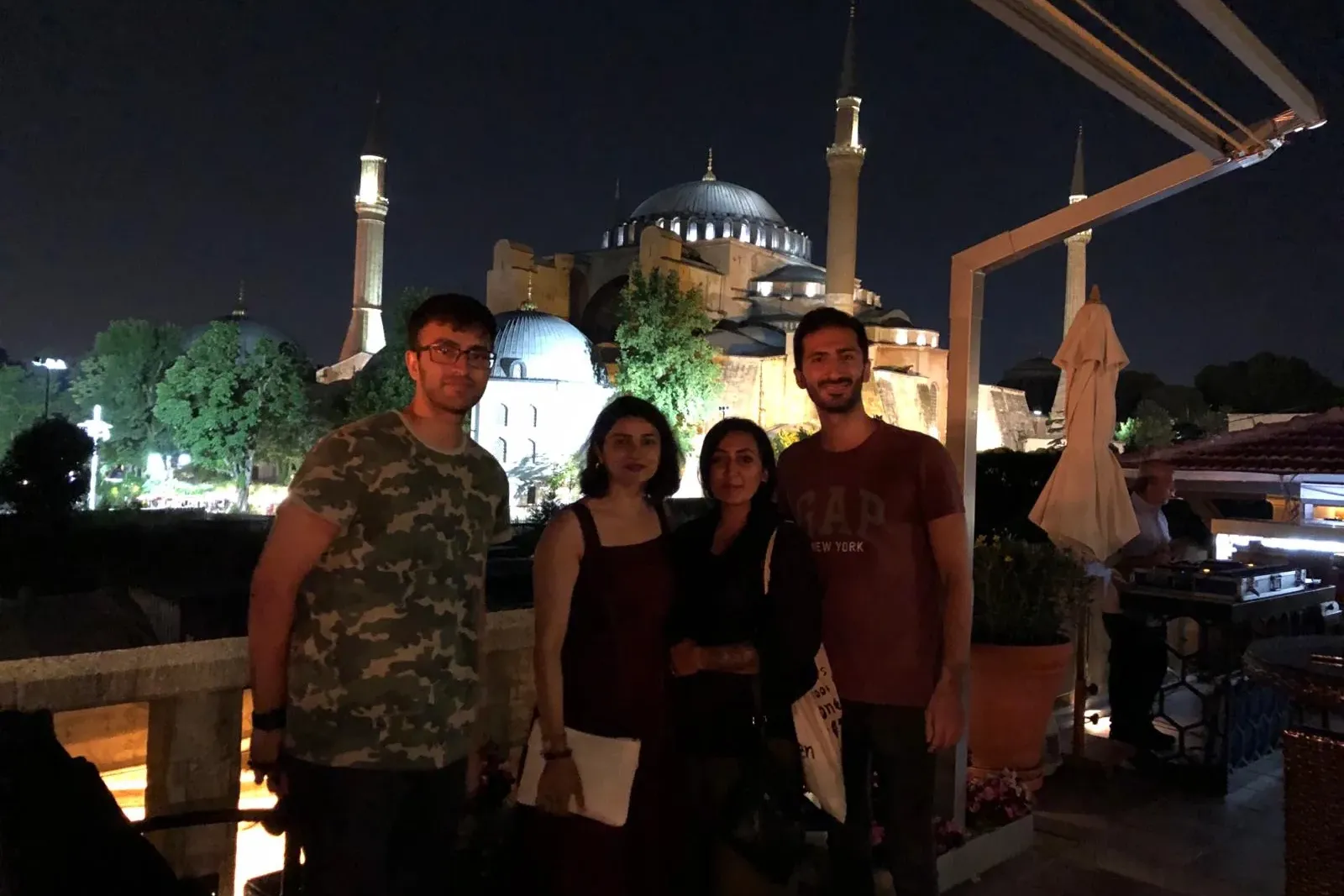Cuatro personas de pie en un balcón de noche, con la iluminada Santa Sofía y sus minaretes al fondo.