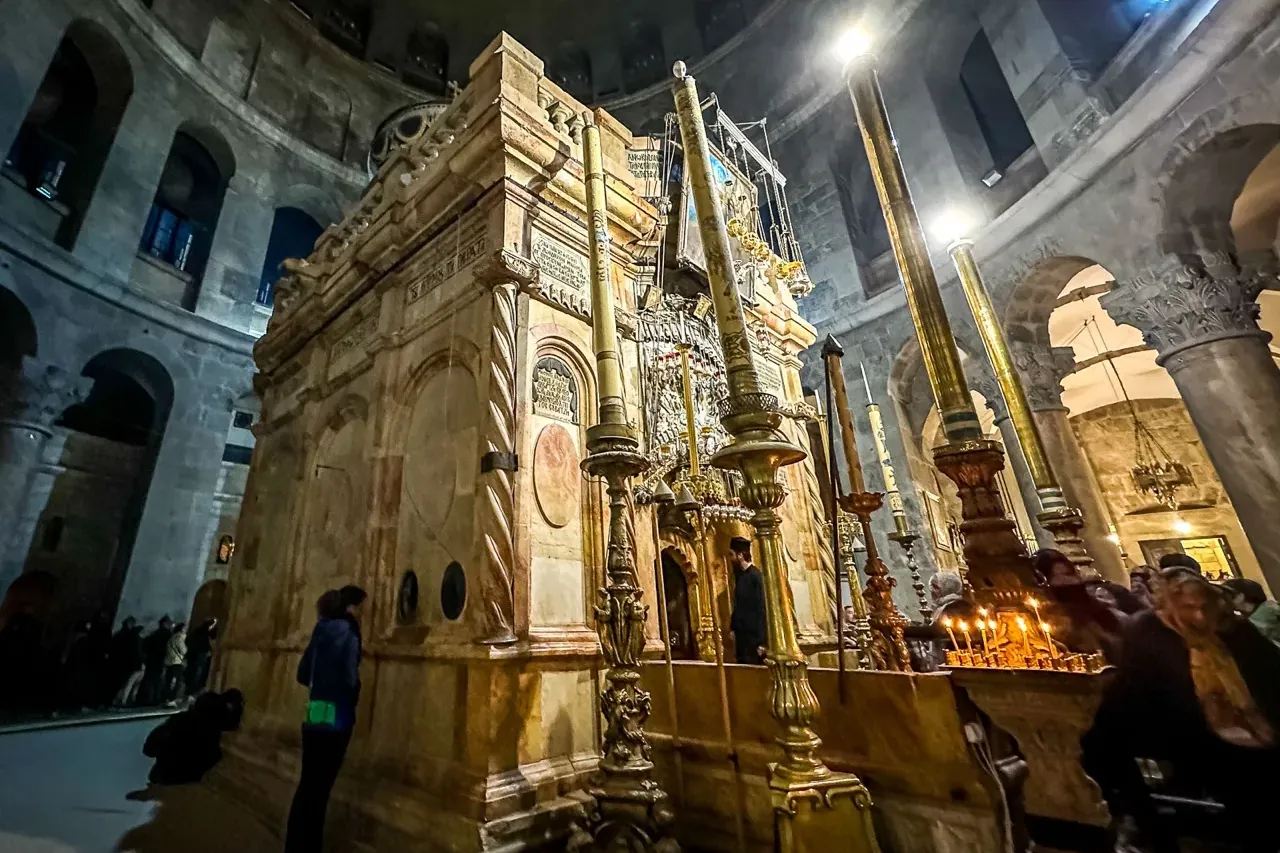 El Edículo de piedra dentro de la Iglesia del Santo Sepulcro, iluminado por altas velas y luces artificiales, con gente al...