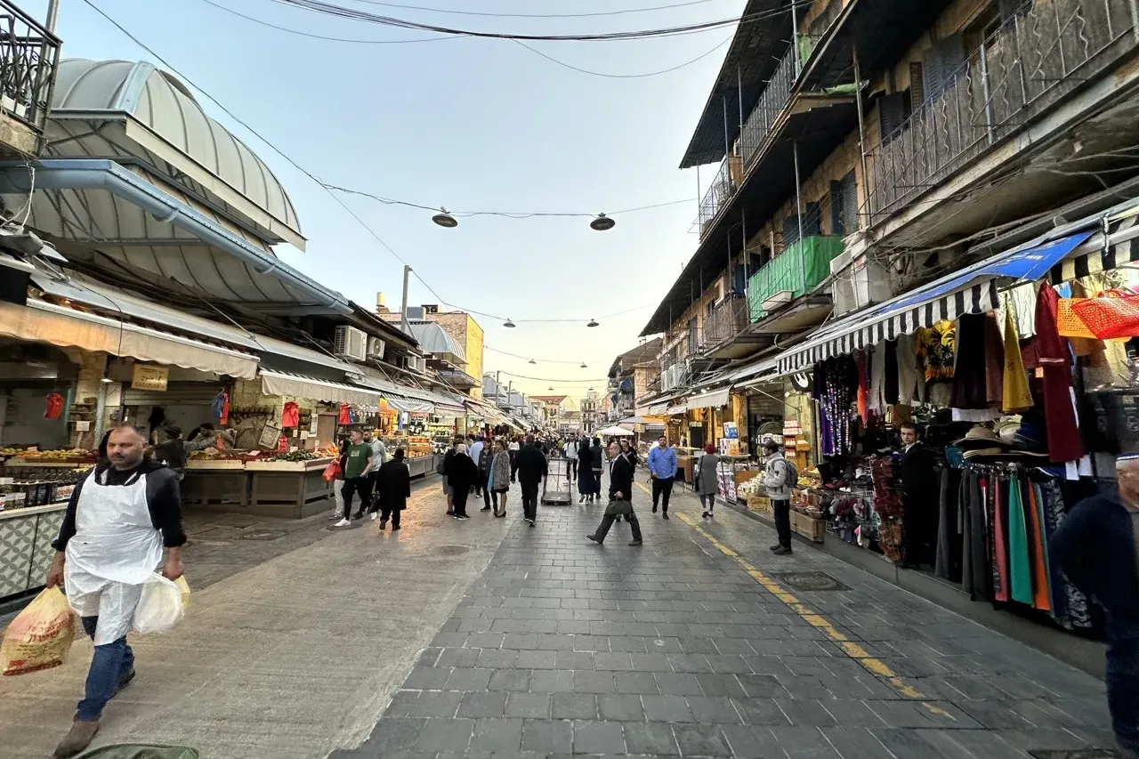 Animada calle de mercado en Jerusalén con puestos de productos y mercancías, gente paseando y edificios de varios pisos ba...