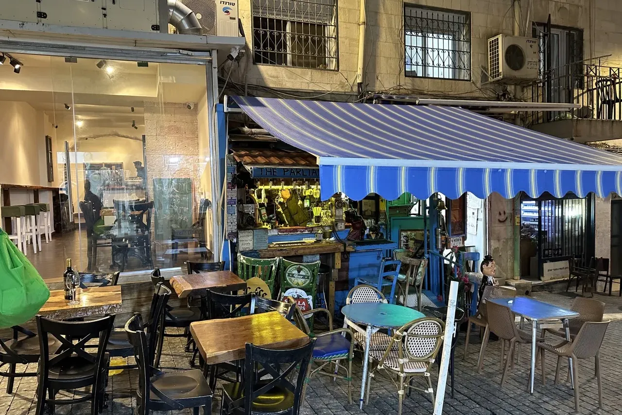 Bar o cafetería al aire libre con mesas y sillas bajo un toldo a rayas azules y blancas de noche. Una fachada de edificio ...
