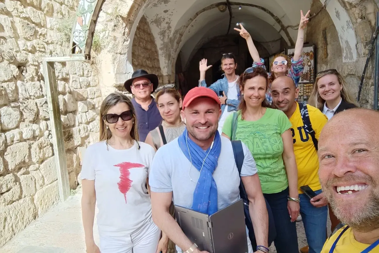 Grupo de turistas sonrientes y un guía haciéndose un selfie en un estrecho callejón de piedra con arcos en la Ciudad Vieja...