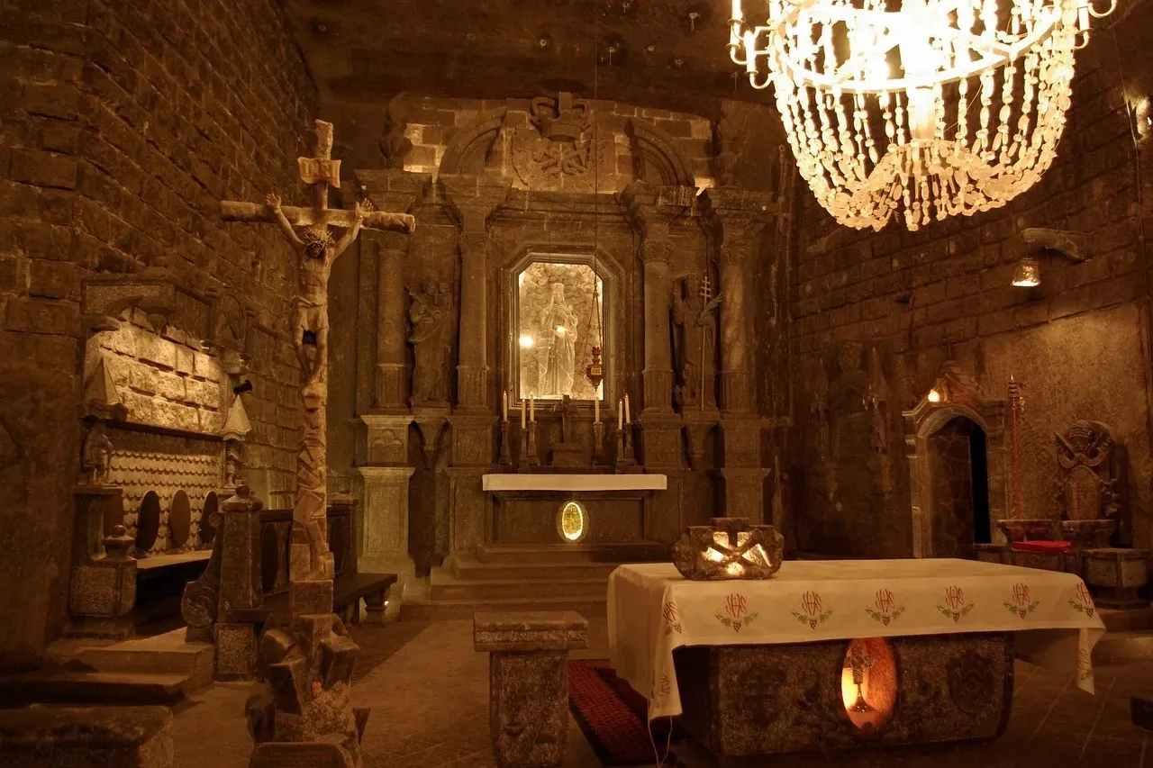 Innenansicht der St.-Kinga-Kapelle in der Salzmine Wieliczka, mit Salzleuchter, Altar, Kruzifix und geschnitzten Figuren.