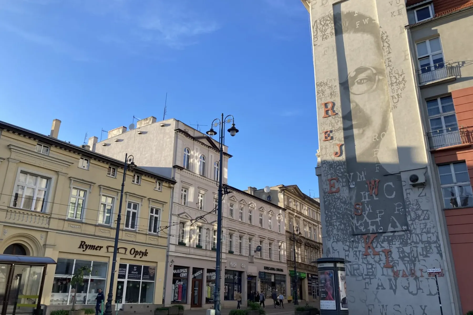 Straßenszene in Bydgoszcz mit historischen Gebäuden, großem Wandgemälde von Mikołaj Rej, Geschäften und einer Straßenbahnh...