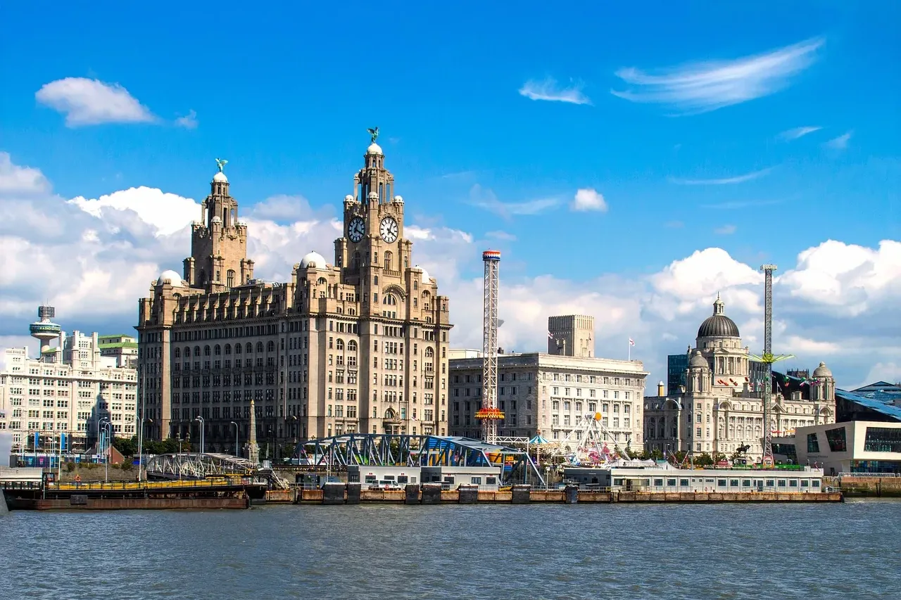 View of Liverpool's waterfront with the Royal Liver Building, other historic structures, and amusement rides under a blue ...