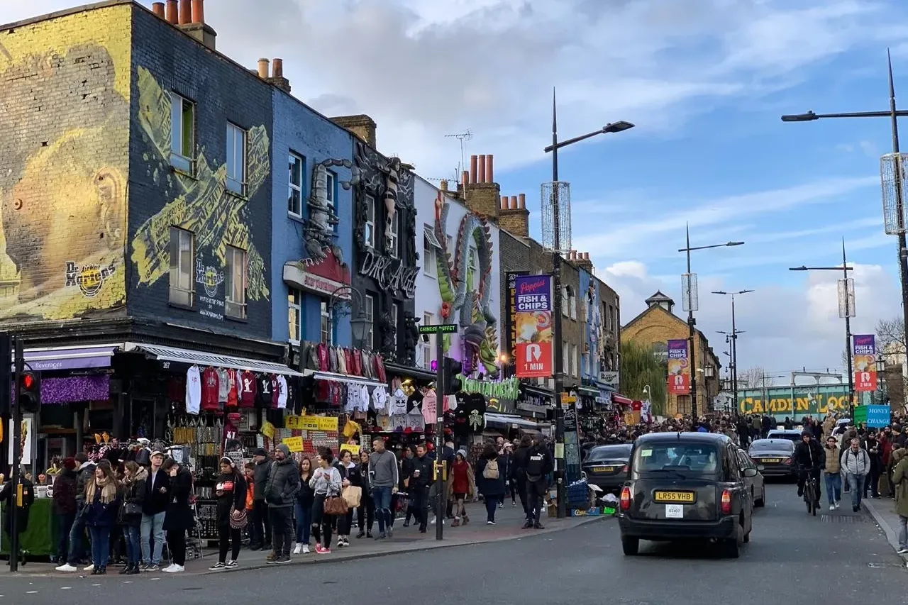 Ulica w Camden Town w Londynie z kolorowymi fasadami sklepów, licznymi pieszymi, czarną taksówką i straganami.