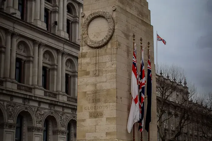 Kamienny pomnik wojenny Cenotaph w Londynie z rzeźbionym wieńcem i napisem "THE GLORIOUS DEAD". Brytyjskie flagi pod szary...