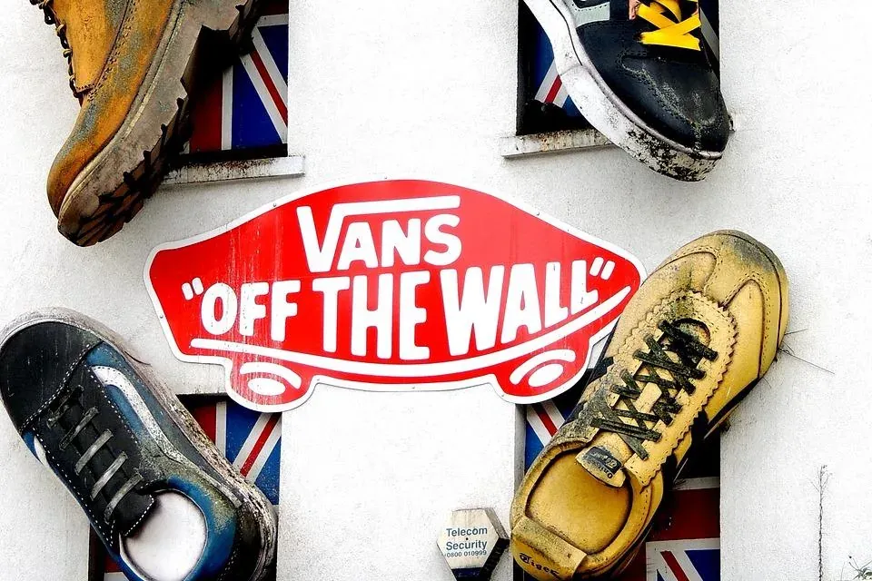 Olbrzymie dekoracyjne buty i czerwony znak 'Vans Off The Wall' na białej ścianie budynku. W oknach widoczne flagi Union Jack.