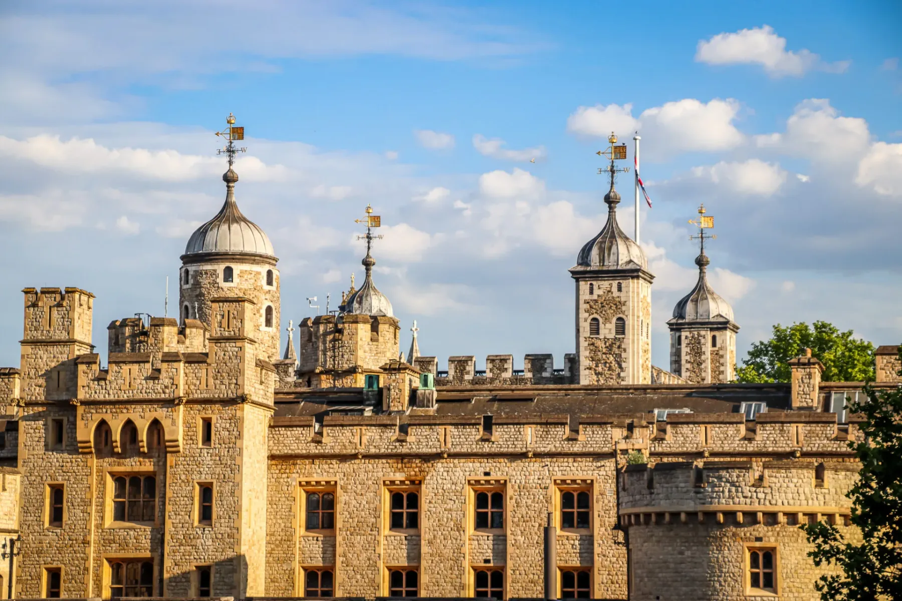 Nahaufnahme der Steinmauern und mehreren grau gekuppelten Türmchen des Tower of London unter blauem Himmel mit weißen Wolken.