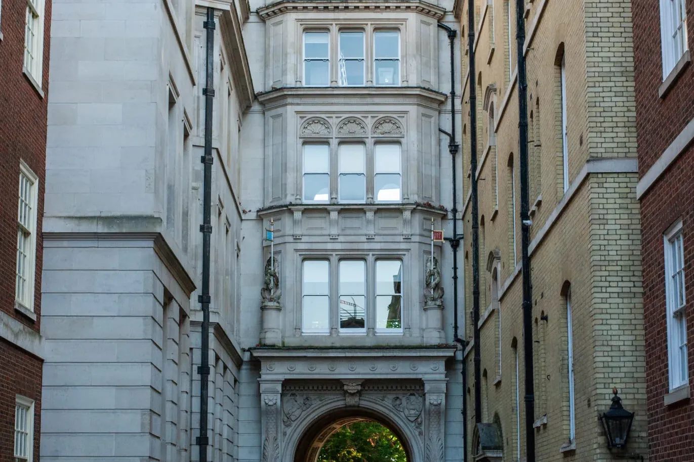 Schmale, gepflasterte Gasse in London, umgeben von historischen Gebäuden. Person mit gelbem Walkative-Regenschirm geht auf...