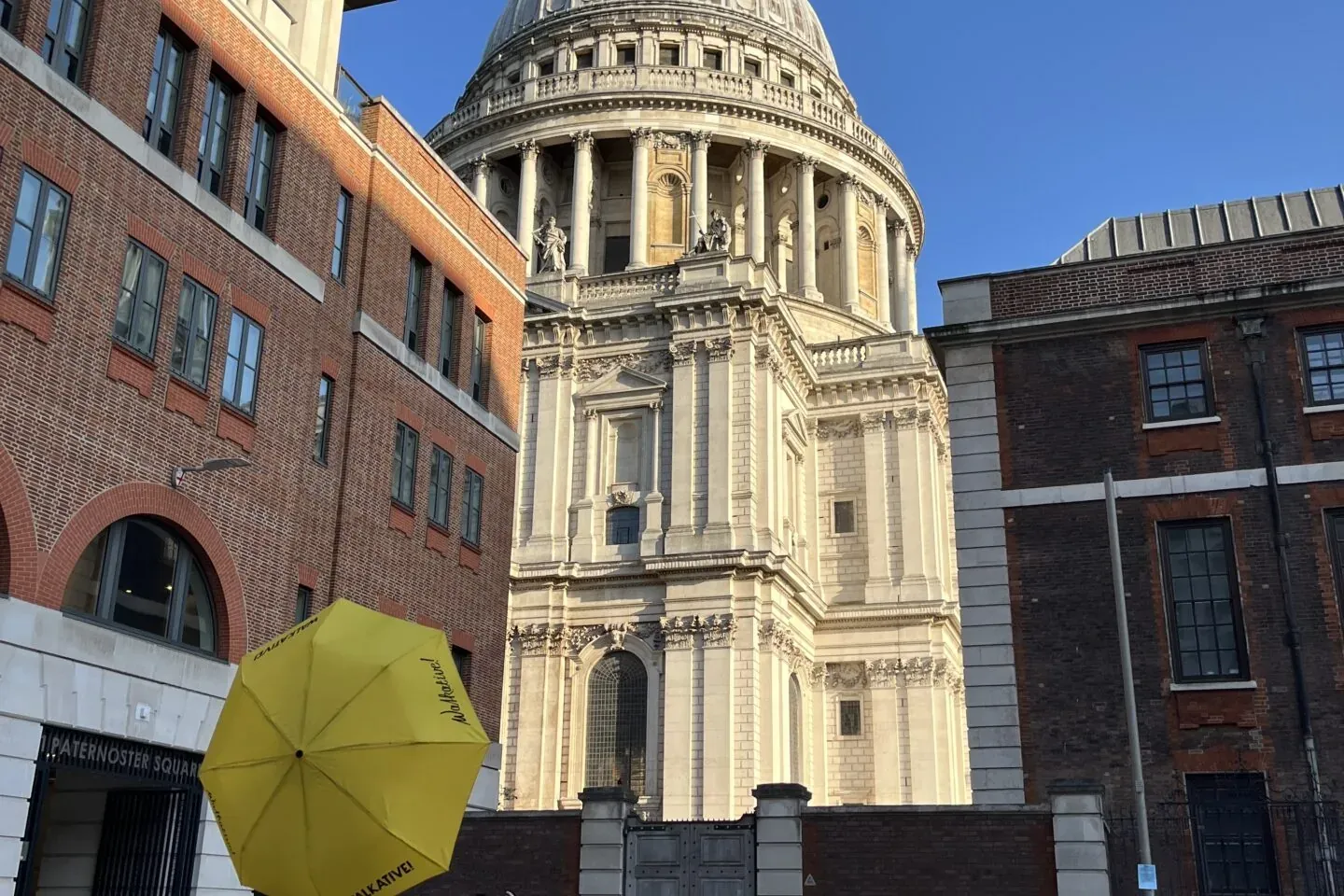Eine Person mit gelbem Walkative-Regenschirm steht vor der St. Paul's Cathedral in London. Paternoster Square im Vordergrund.