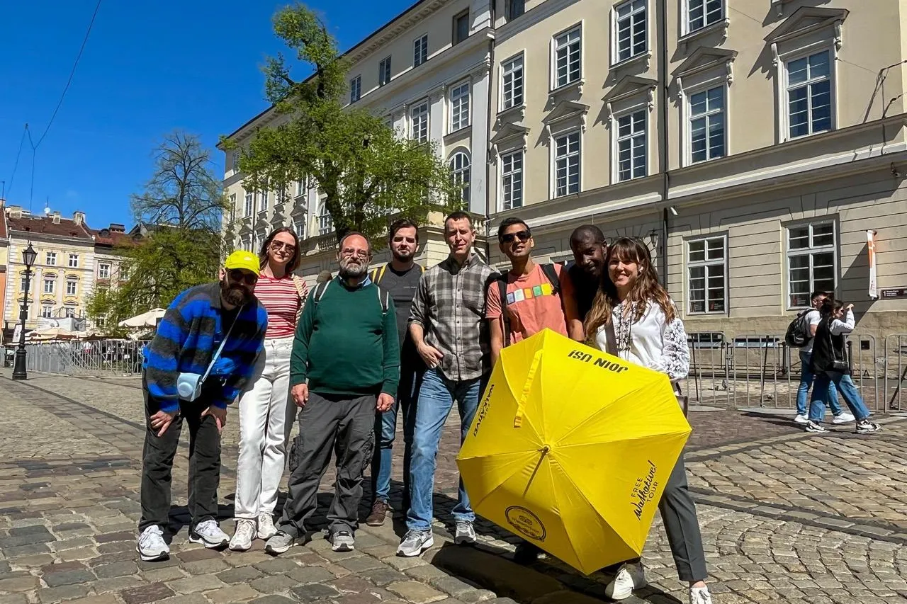 A diverse group of seven people on a cobblestone street in Lviv, with a guide holding a yellow Walkative umbrella in front...