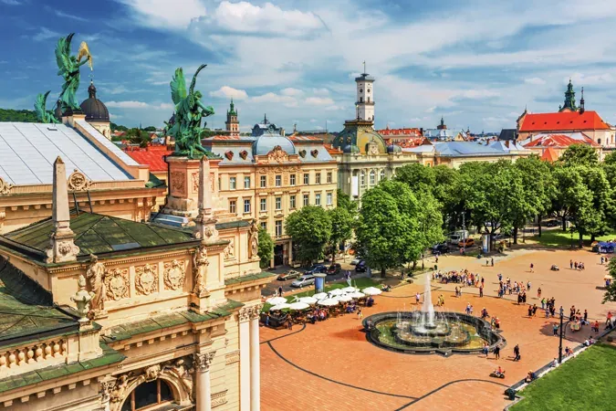 Aerial view of Lviv city center with the Opera House, a busy square with a round fountain, trees, and historic buildings u...