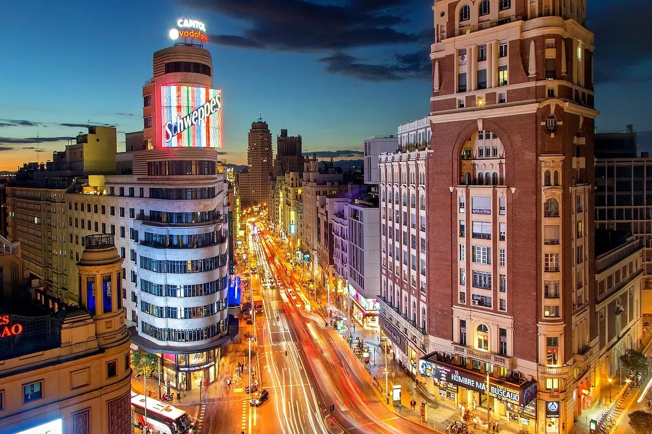 Calle Gran Vía en Madrid de noche, con el letrero de Schweppes del Edificio Capitol y estelas de luz de vehículos.