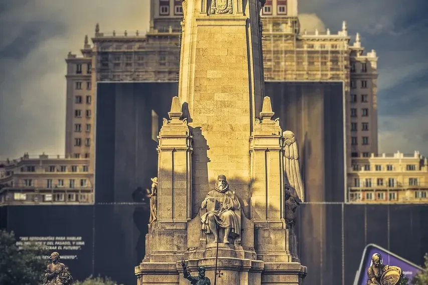 Gran monumento de piedra a Cervantes, con estatuas ecuestres de Don Quijote y Sancho Panza, y un edificio al fondo.