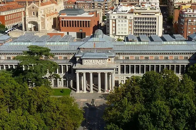 Vista aérea del Museo del Prado en Madrid, un gran edificio neoclásico con pórtico de columnas, rodeado de árboles verdes.
