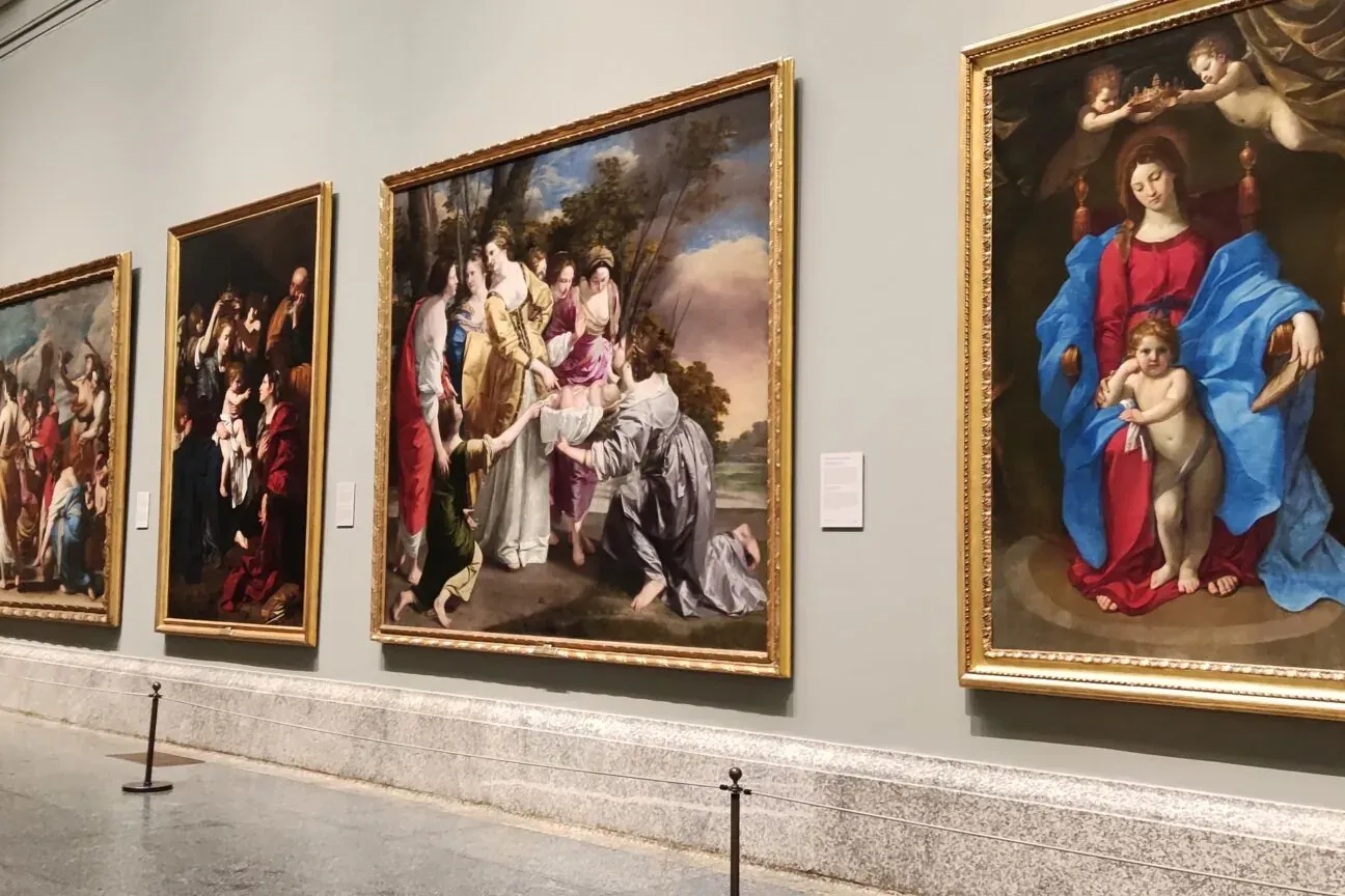 Cuatro grandes cuadros clásicos enmarcados cuelgan de una pared gris clara de museo, con cuerdas y postes en el suelo.