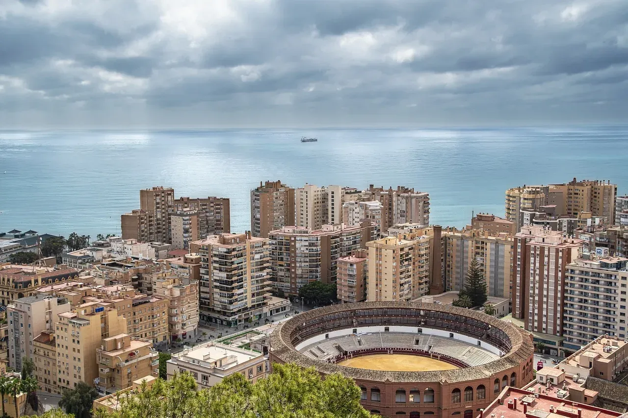 Luftaufnahme der Küste Malagas mit der Stierkampfarena Plaza de Toros im Vordergrund, Wohngebäuden und dem Meer unter bewö...