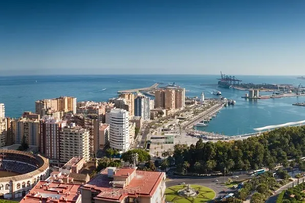 Panoramablick auf Malagas Stadtbild mit der Stierkampfarena La Malagueta, dem Hafen und dem Mittelmeer unter blauem Himmel.
