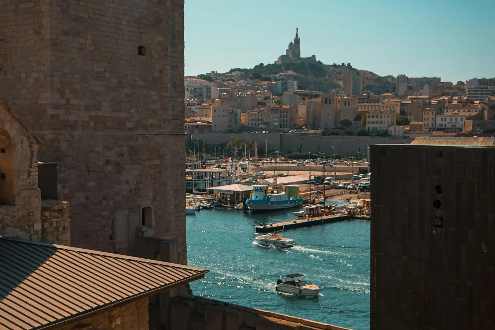 Vista desde una fortaleza de piedra al Puerto Viejo de Marsella con barcos y la basílica Notre-Dame de la Garde en la colina.