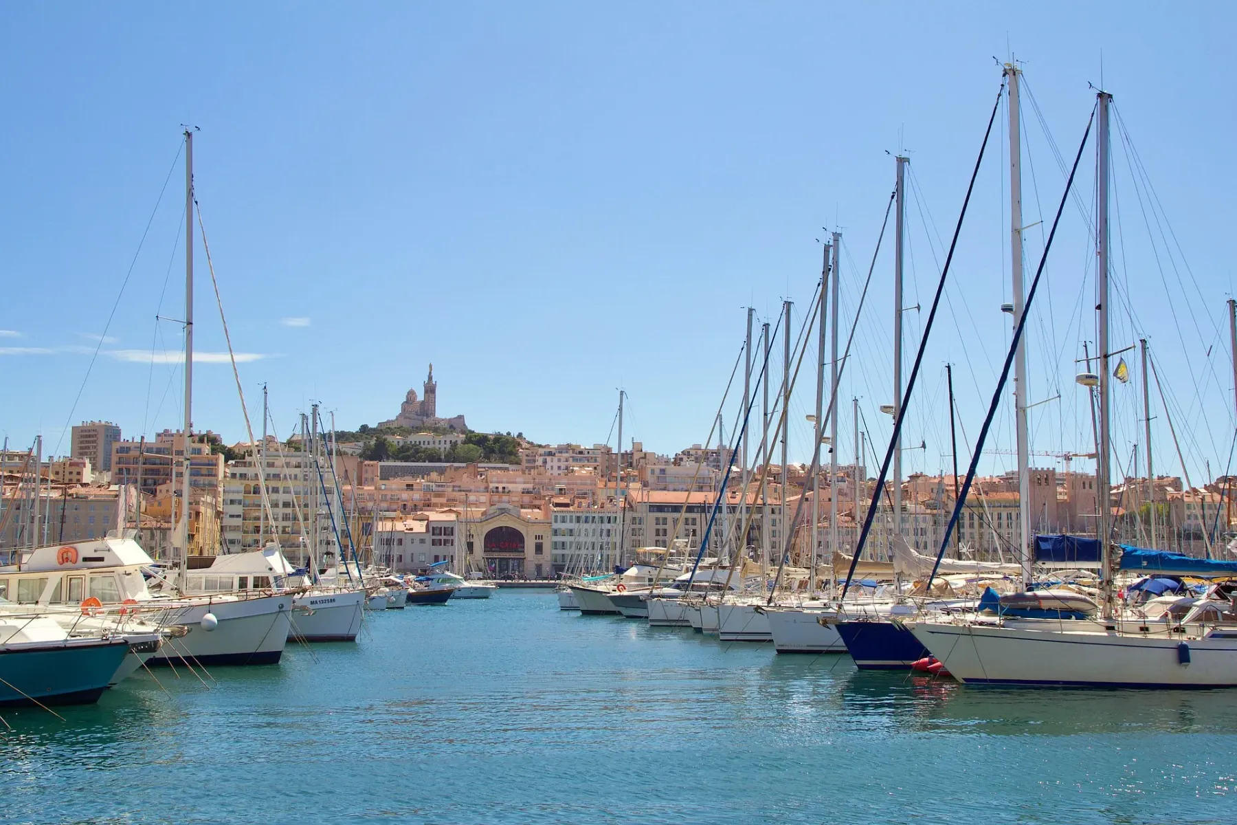Puerto de Marsella con veleros y la basílica de Notre-Dame de la Garde al fondo.