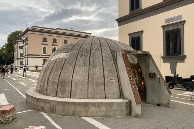 Kopułowy budynek dawnego bunkra, obecnie muzeum, ze szklanym wejściem z napisem „MUSEUM” przy ulicy miasta.