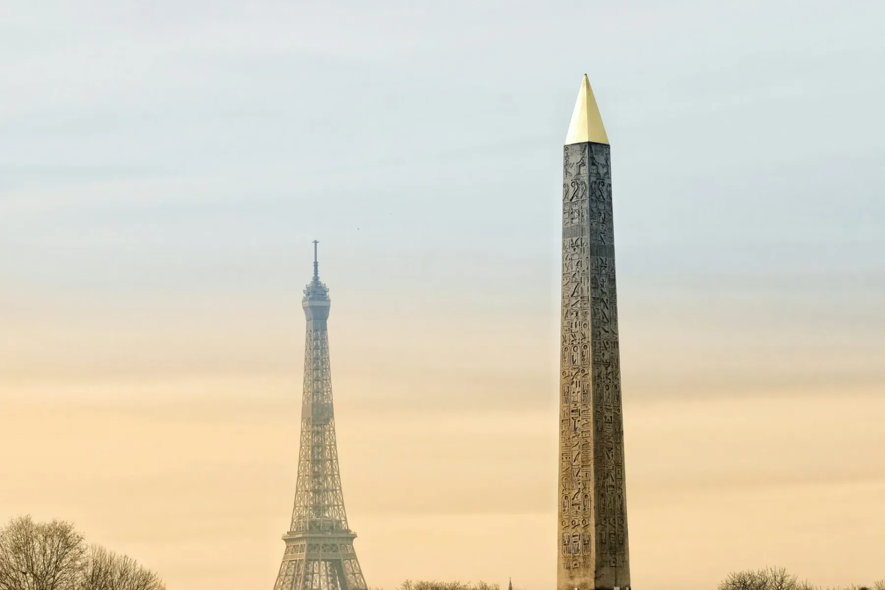 Der Obelisk von Luxor mit goldener Spitze und Hieroglyphen, im Hintergrund der obere Teil des Eiffelturms bei diesigem Him...