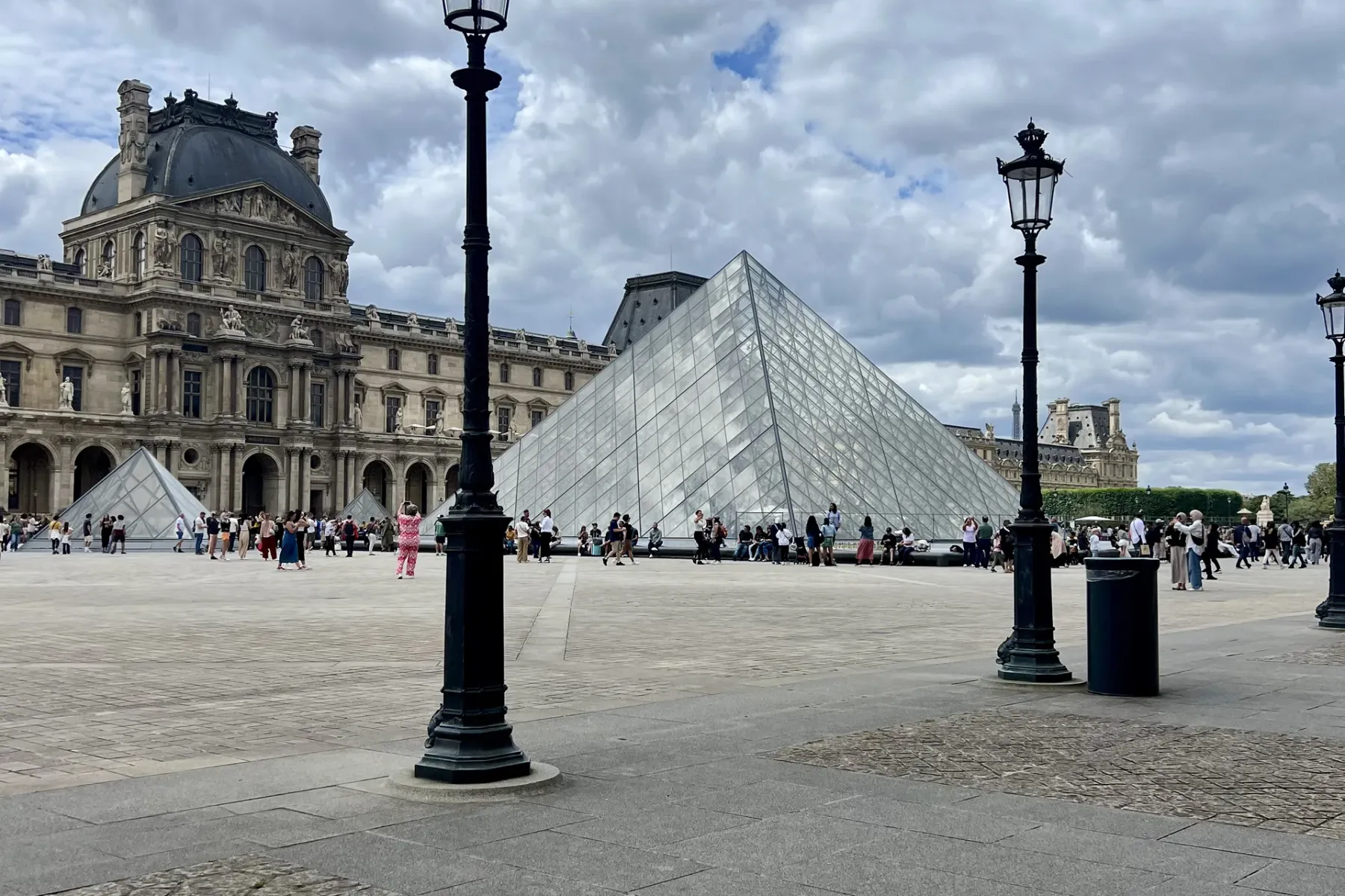 Die Glaspyramide des Louvre-Museums in Paris, mit dem historischen Palastgebäude im Hintergrund und Menschen auf dem Platz.