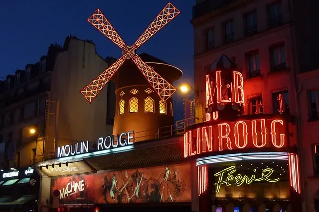 Das Moulin Rouge Kabarettgebäude bei Nacht, beleuchtet mit lebhaften roten Neonschildern und einer leuchtenden roten Windm...