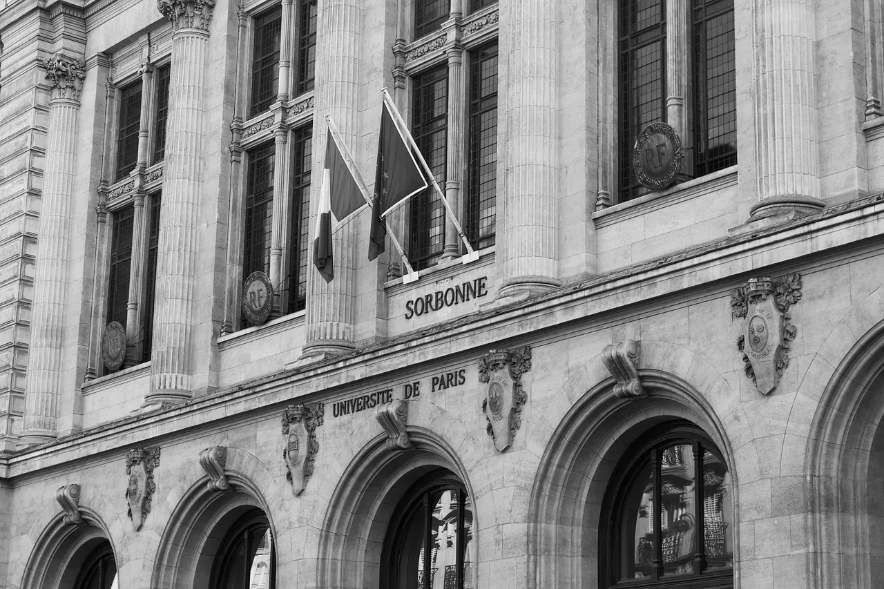 Schwarz-Weiß-Detailansicht der Fassade der Universität Sorbonne in Paris, mit Säulen, Bogenfenstern und Flaggen.