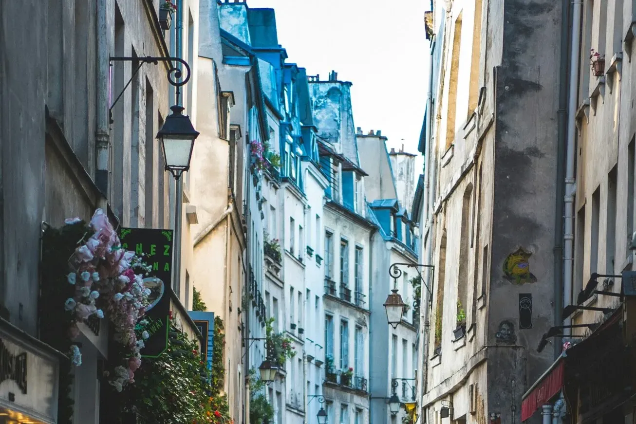 Eine enge Kopfsteinpflasterstraße in Paris mit alten Gebäuden, Ladenfronten und zwei Personen in der Ferne.
