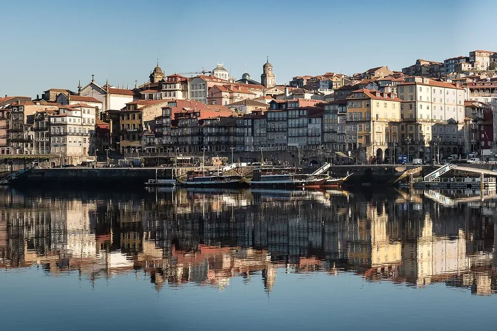 Historische, mehrstöckige Gebäude mit roten Dächern am Fluss, die sich im ruhigen Wasser spiegeln. Traditionelle Boote lie...