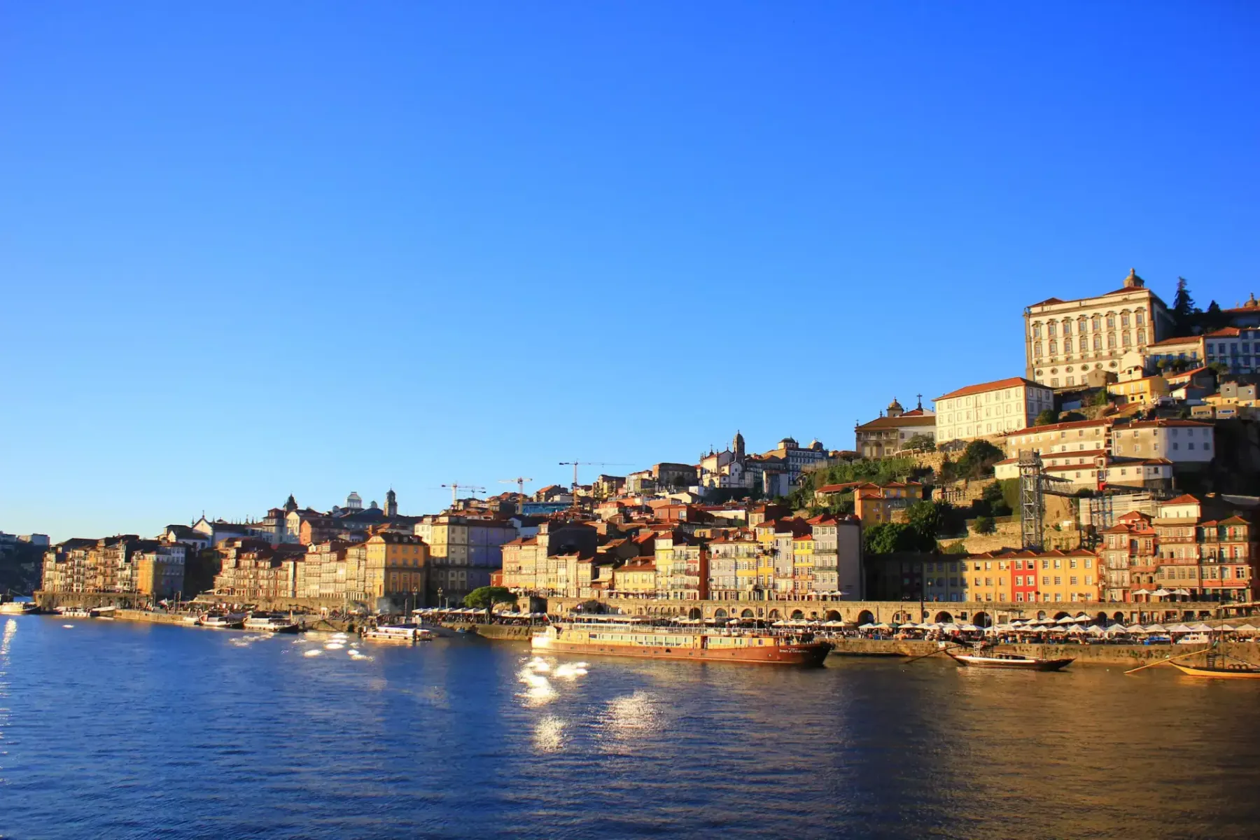 Distrito de la Ribeira de Oporto con edificios coloridos descendiendo una colina hacia el río Duero, barcos amarrados.